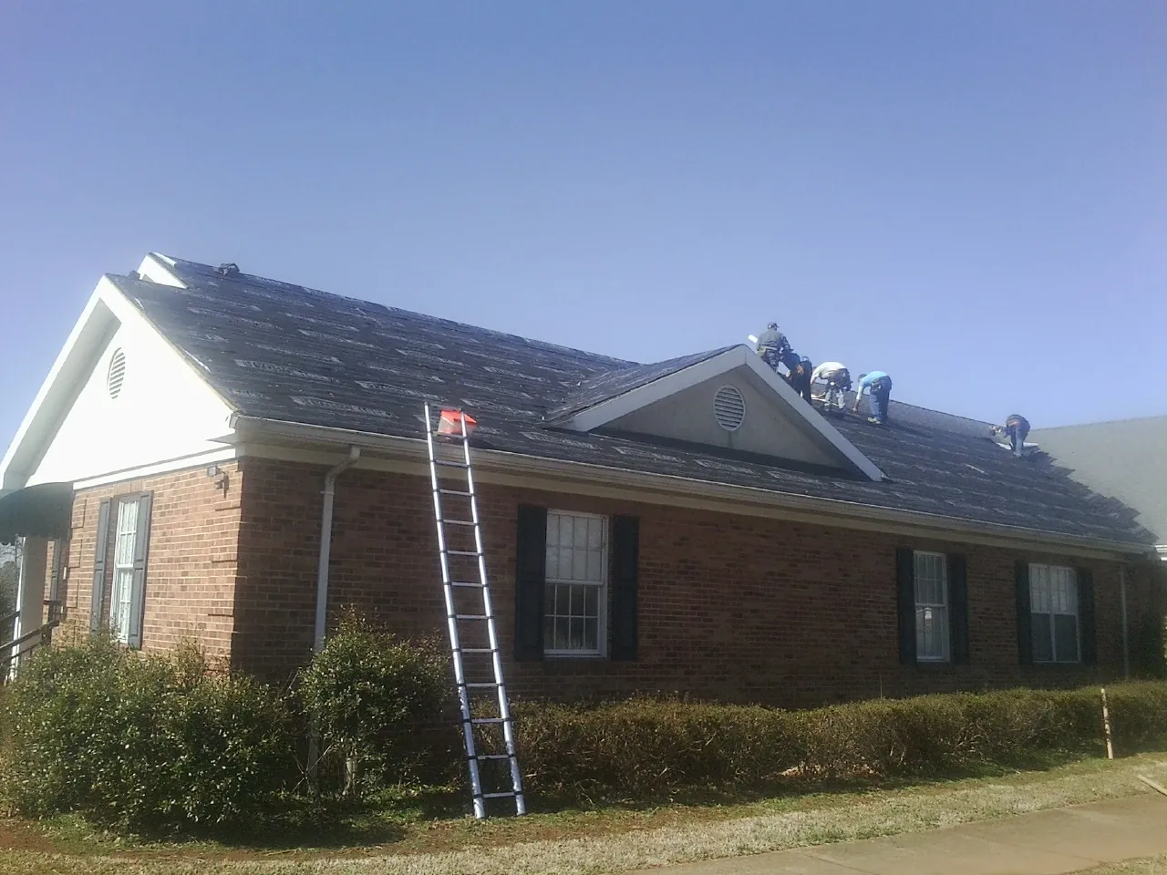 Crew tearing shingles off a brick ranch roof with a ladder set — Emergency Roof Repair work by our crew in Whitehouse Station