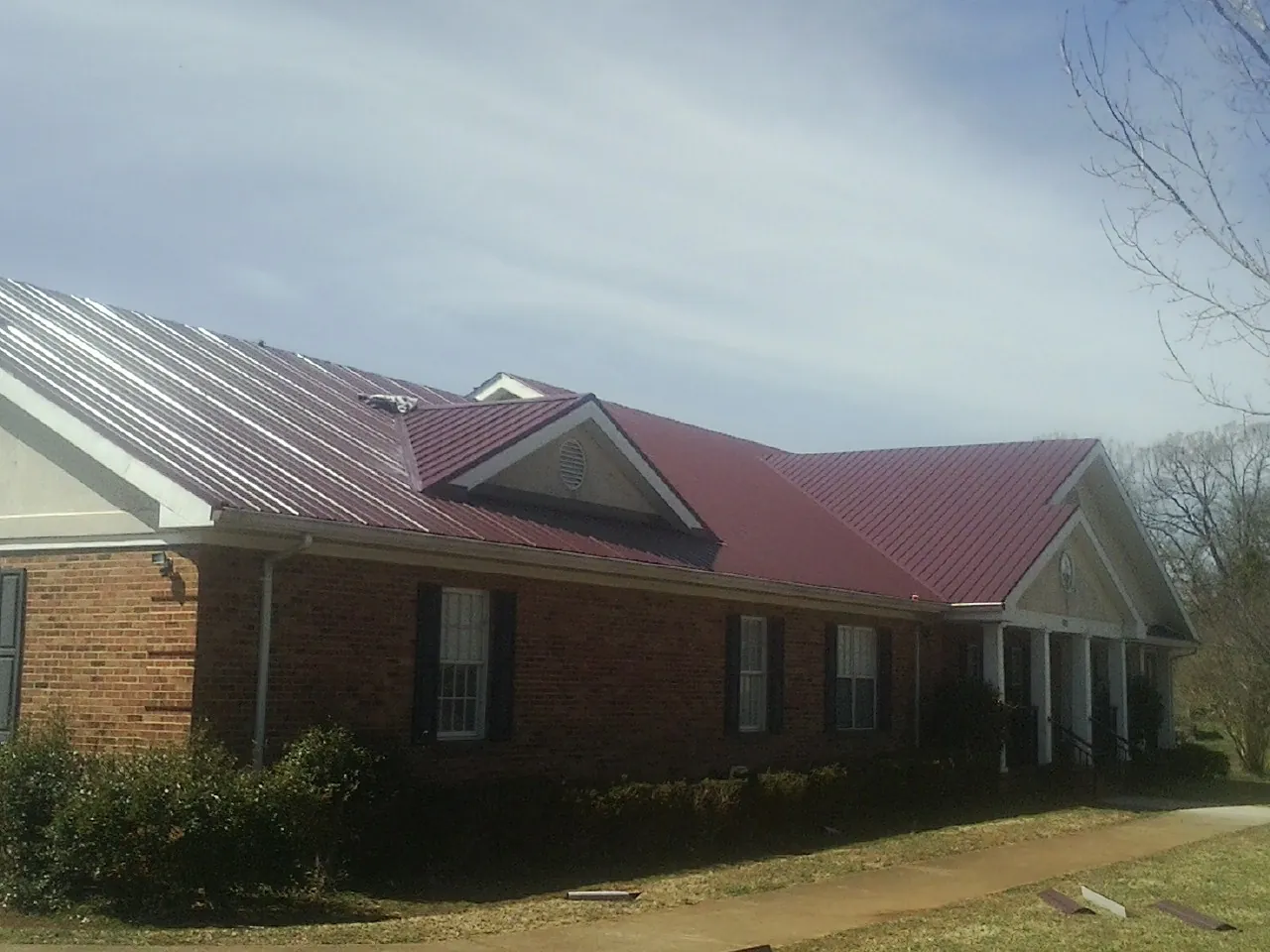 Red metal roof with gabled entries on a long brick building, from a Hail Damage Roof Repair job in Whitehouse Station