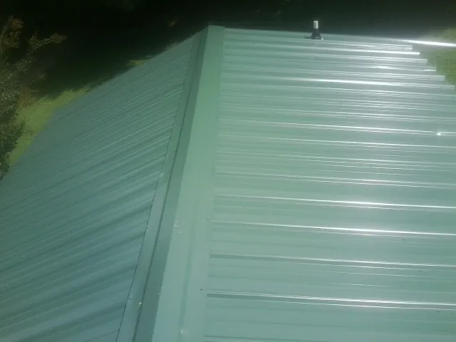New green metal panels meeting at the ridge of a roof — Flat Roof Repair work by our crew in Whitehouse Station