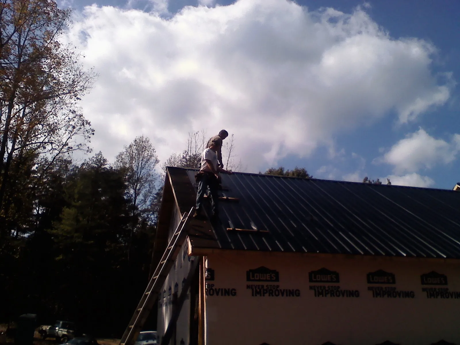 Roofer fastening dark metal panels high against a cloudy sky, from a Roof Inspection job in Whitehouse Station