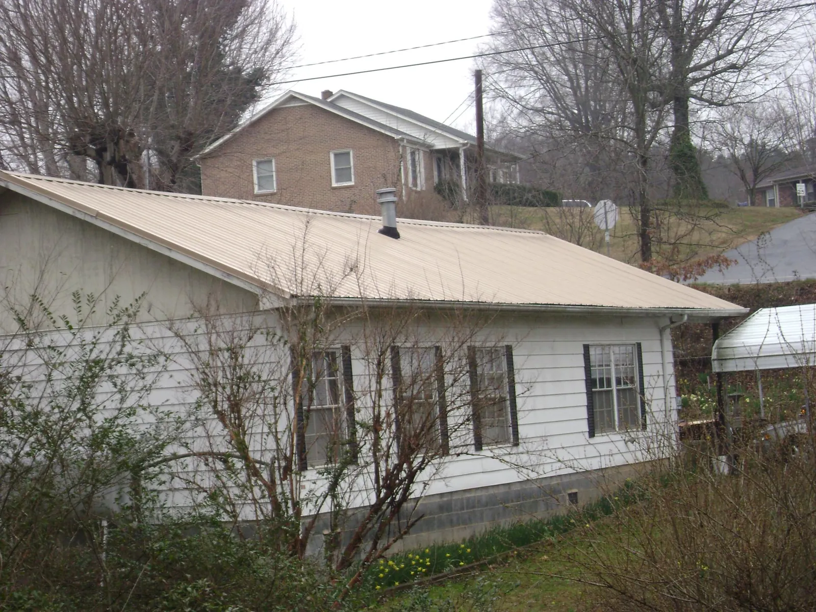 Tan metal roof on a white sided house set into a hillside — Commercial Roofing by Roofing Brothers in Whitehouse Station